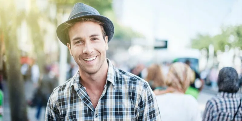 A young man wearing a fedora in a park.