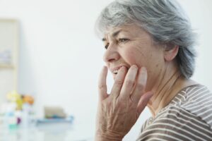 An older woman grabbing her jaw in pain after breaking a tooth.