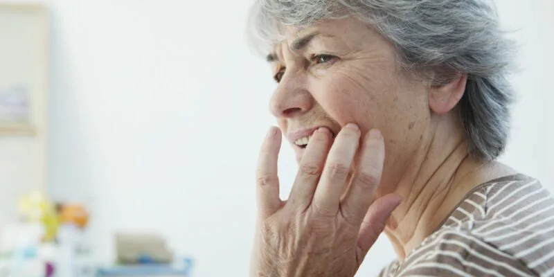 An older woman grabbing her jaw in pain after breaking a tooth.