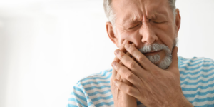 A man clutching his jaw in pain from an untreated dental infection in need of a root canal.