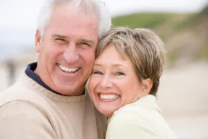 A smiling older couple on the beach after restorative dental treatments in Casper.