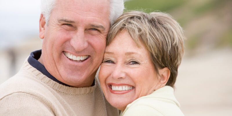 A smiling older couple on the beach after restorative dental treatments in Casper.